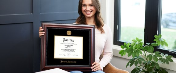 A student holding a diploma frame next to window.