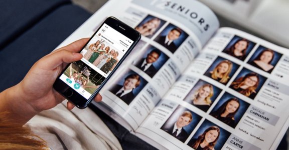 A student using Yearbook+ on their phone next to their yearbook.